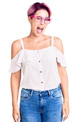 Young beautiful woman with pink hair wearing casual clothes and glasses winking looking at the...