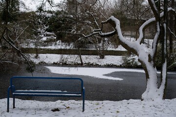 metal bench in the snowy park in front of a frozen pond