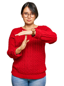 Young beautiful hispanic woman with short hair wearing casual sweater and glasses doing time out gesture with hands, frustrated and serious face