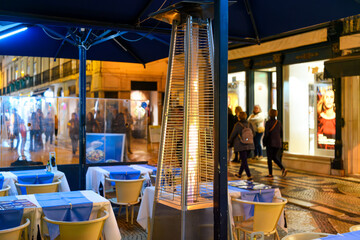 A burning gas flame heater warms tables at a sidewalk cafe at night in the touristic main shopping...