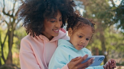 Mother daughter holding mobile phone looking cartoon at sunny nature close up.