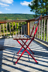A chair with red legs standing on a wooden deck with a tree covered mountainside in the background.