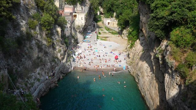Magnificent top view from Fjord Furore Bridge to people relaxing and swimming on beach in Amalfi Coast on summer sunny day. Scenic vacation destination for tourists on Amalfi Coast in Italy.