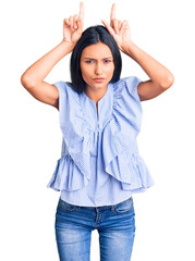 Young beautiful latin girl wearing casual clothes doing funny gesture with finger over head as bull...