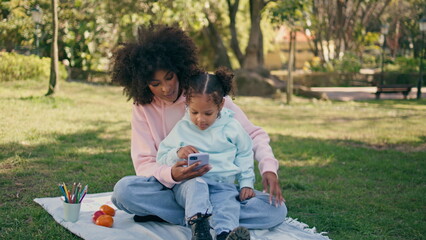 Mother daughter playing telephone on grass meadow. Woman showing phone to girl