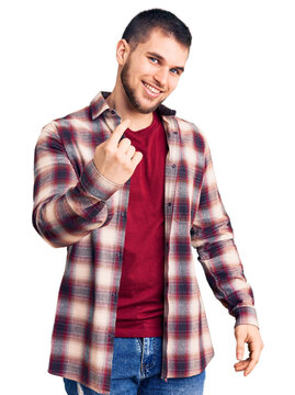 Young handsome man wearing casual shirt beckoning come here gesture with hand inviting welcoming happy and smiling