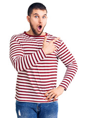 Young handsome man wearing striped sweater surprised pointing with finger to the side, open mouth amazed expression.