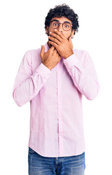 Handsome young man with curly hair and bear wearing business clothes shocked covering mouth with hands for mistake. secret concept.