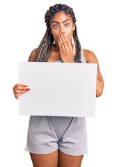 Young african american woman with braids holding blank empty banner covering mouth with hand, shocked and afraid for mistake. surprised expression