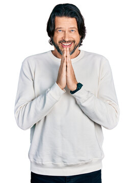 Middle age caucasian man wearing casual clothes praying with hands together asking for forgiveness smiling confident.