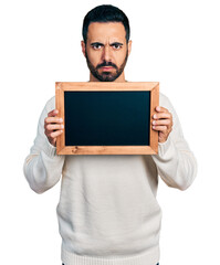 Young hispanic man with beard holding blackboard skeptic and nervous, frowning upset because of problem. negative person.