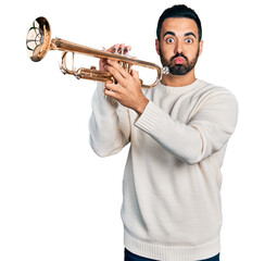 Young hispanic man with beard playing trumpet puffing cheeks with funny face. mouth inflated with...