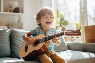 Cute little boy learning to play guitar in living room. Child having fun with music instrument. Art...