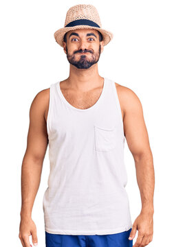 Young hispanic man wearing casual summer hat puffing cheeks with funny face. mouth inflated with air, crazy expression.