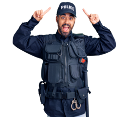 Young hispanic man wearing police uniform smiling amazed and surprised and pointing up with fingers and raised arms.