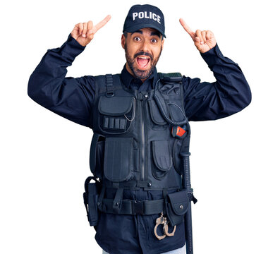 Young hispanic man wearing police uniform smiling amazed and surprised and pointing up with fingers and raised arms.