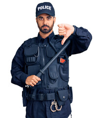 Young hispanic man wearing police uniform holding baton with angry face, negative sign showing dislike with thumbs down, rejection concept
