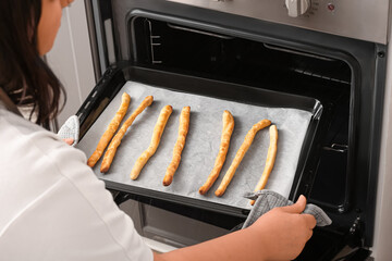 Woman pulling baking tray with prepared Italian Grissini from oven