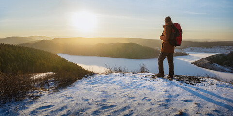 Man hiker with backpack standing on top of hill and enjoying looking at sunset. freedom hiking in...
