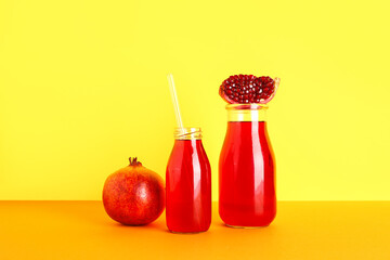 Bottles of fresh pomegranate juice on yellow background
