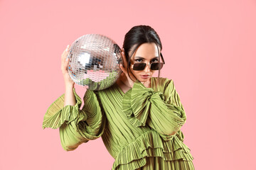 Fashionable beautiful woman in green dress and sunglasses with disco ball posing on pink background