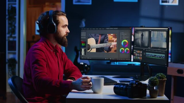 Videographer using editing software to assemble footage into cohesive final result while enjoying cup of coffee. Specialist color correcting clips while listening music in headphones