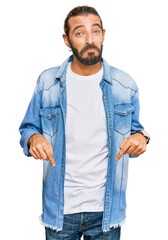 Attractive man with long hair and beard wearing casual denim jacket pointing down looking sad and...