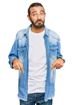 Attractive man with long hair and beard wearing casual denim jacket pointing down looking sad and upset, indicating direction with fingers, unhappy and depressed.