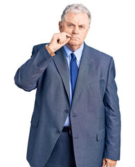 Senior grey-haired man wearing business jacket mouth and lips shut as zip with fingers. secret and...