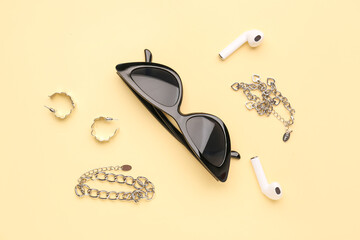 Composition with stylish sunglasses, modern earphones and jewelry on beige background