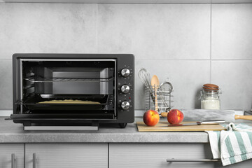 Open electric oven with dough on countertop in kitchen