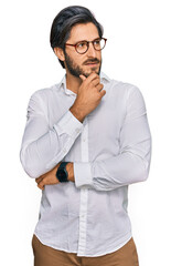 Young hispanic man wearing business shirt and glasses with hand on chin thinking about question, pensive expression. smiling with thoughtful face. doubt concept.