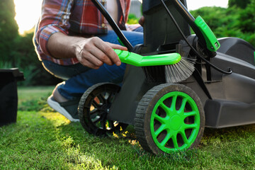 Man cleaning lawn mower with brush in garden, closeup