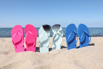 Stylish colorful flip flops and sunglasses on beach sand