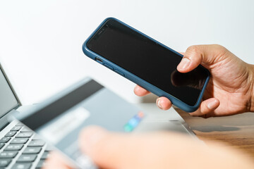 Close up male hand holding a bank credit card doing online transactions using a laptop and smart phone