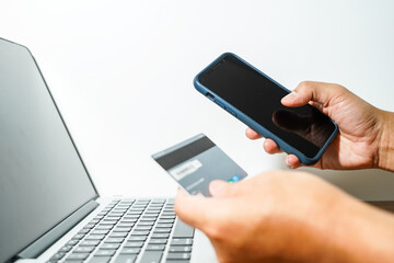 Close up male hand holding a bank credit card doing online transactions using a laptop and smart phone