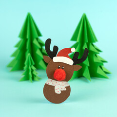 Handmade cute reindeer with fir trees made from paper on blue background