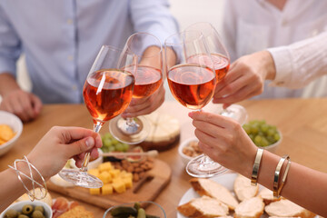 People clinking glasses with rose wine above wooden table indoors, closeup