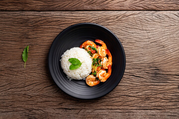 Stir-fried shrimp with basil Thai street food arranged on a black plate Spicy Thai food placed on a wooden table. Top view.