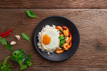 Stir-fried shrimp with basil Thai street food arranged on a black plate with a fried egg Spicy Thai food placed on a wooden table. Top view.