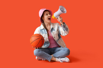Young woman with ball shouting into megaphone on red background