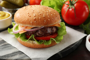 Tasty hamburger with patty, cheese and vegetables on wooden table, closeup