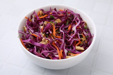 Tasty salad with red cabbage and walnuts in bowl on white tiled table, closeup