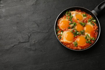 Delicious Shakshuka in frying pan on black textured table, top view. Space for text