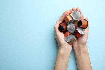 Woman holding heap of coffee capsules on light blue background, top view. Space for text