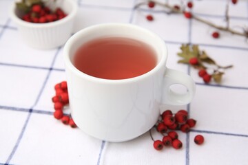 Obraz na płótnie Canvas Cup with hawthorn tea and berries on table, closeup