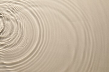 Fototapeta na wymiar Rippled surface of clear water on beige background, top view