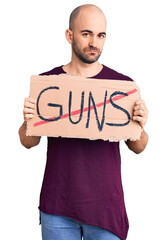 Young handsome man holding prohibited guns banner thinking attitude and sober expression looking self confident