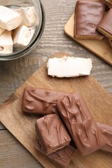 Tasty chocolate bars and nougat on wooden table, flat lay