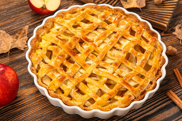 Baking dish with delicious apple pie and cinnamon on wooden background